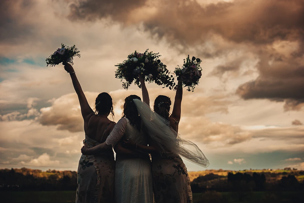 Bride and her bridesmaids lift bouquets in the air at The Ashes Barns Staffordshire